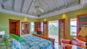 A bedroom with a bed, a television, a seating area, and a balcony with a view. - A Yacht Haven (Christiansted)