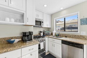 Une cuisine moderne avec des meubles blancs, une cuisinière à gaz, un four à micro-ondes, une machine à café et un lave-vaisselle.