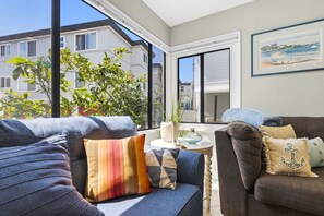 A modern living room with a sofa, a coffee table, and a view of a building through a large window.