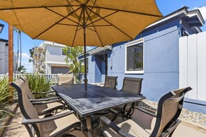 An outdoor patio with a table and chairs, a large umbrella, and a view of a blue building.