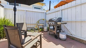 Un patio exterior con una parrilla, sillas y una mesa.