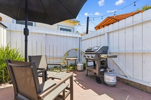 An outdoor patio with a grill, chairs, and a table.