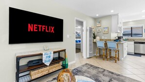 Un moderno salón con un televisor de pantalla plana grande que muestra 'NETFLIX' en letras rojas.