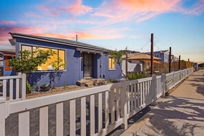 A row of modern houses with a white picket fence, a clear sky, and a sunset.