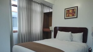 A hotel room with a large bed, a brown throw blanket, a painting on the wall, and a window with curtains. - Hotel Seven Mapi Machupicchu (Machu Picchu)