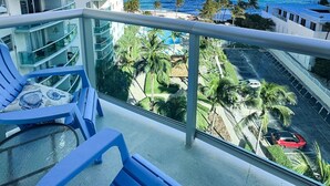 En balkon med blå stole og udsigt over havet samt en hotelbygning.