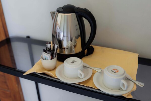 A table with a coffee maker, two cups, and a spoon on a tray.