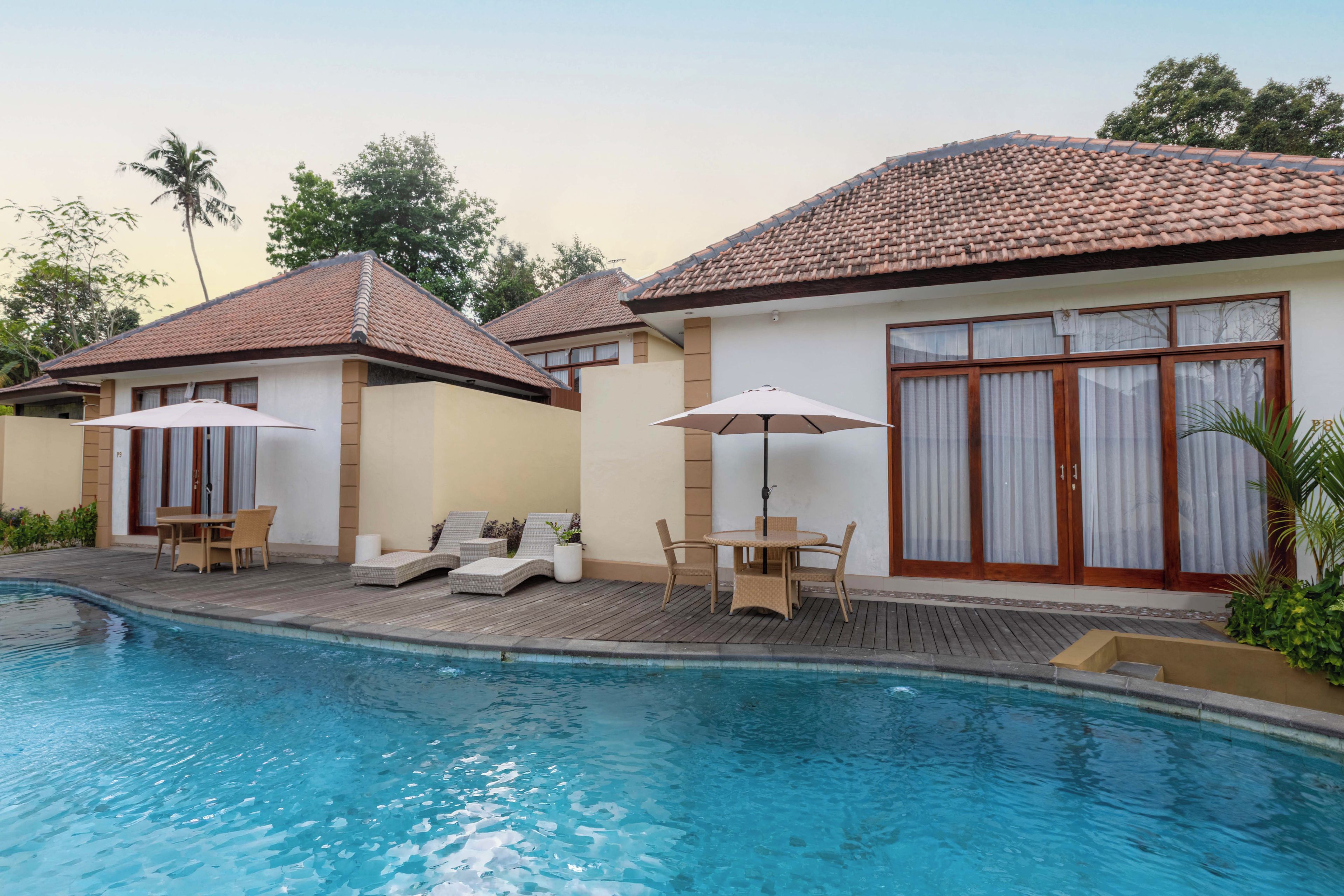 A poolside area with lounge chairs and umbrellas, a tiled roof, and a large window with curtains.