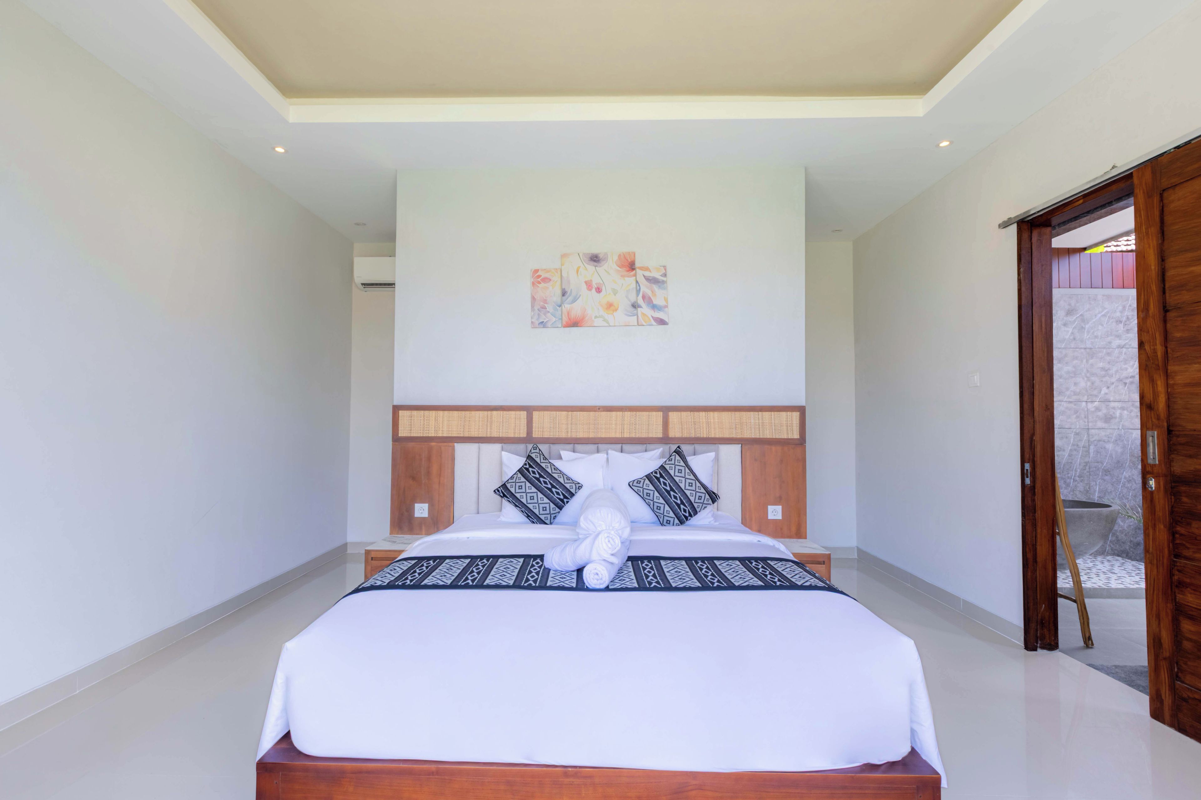 Une chambre spacieuse avec un grand lit, une tête de lit en bois et une petite œuvre d’art accrochée au mur.