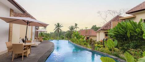 A pool area with lounge chairs and umbrellas, surrounded by lush greenery and tropical plants.