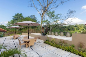 An outdoor patio with tables and chairs, surrounded by greenery and a clear sky. - The green Sidemen  (Klungkung)