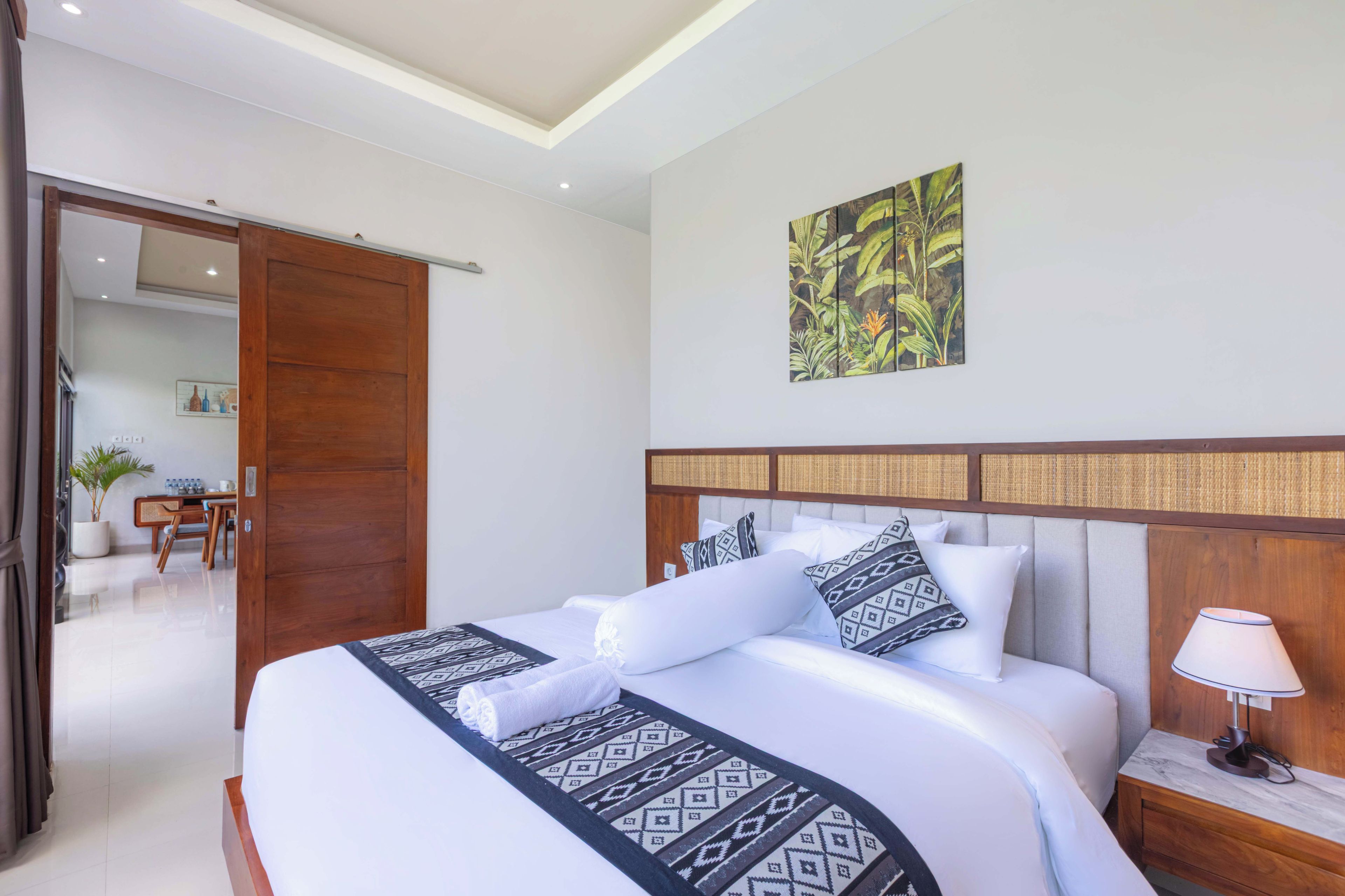 A hotel room with a large bed, a wooden headboard, a wall-mounted artwork, and a desk with a chair.