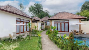 A row of single-story villas with tiled roofs, a swimming pool, and outdoor seating areas.