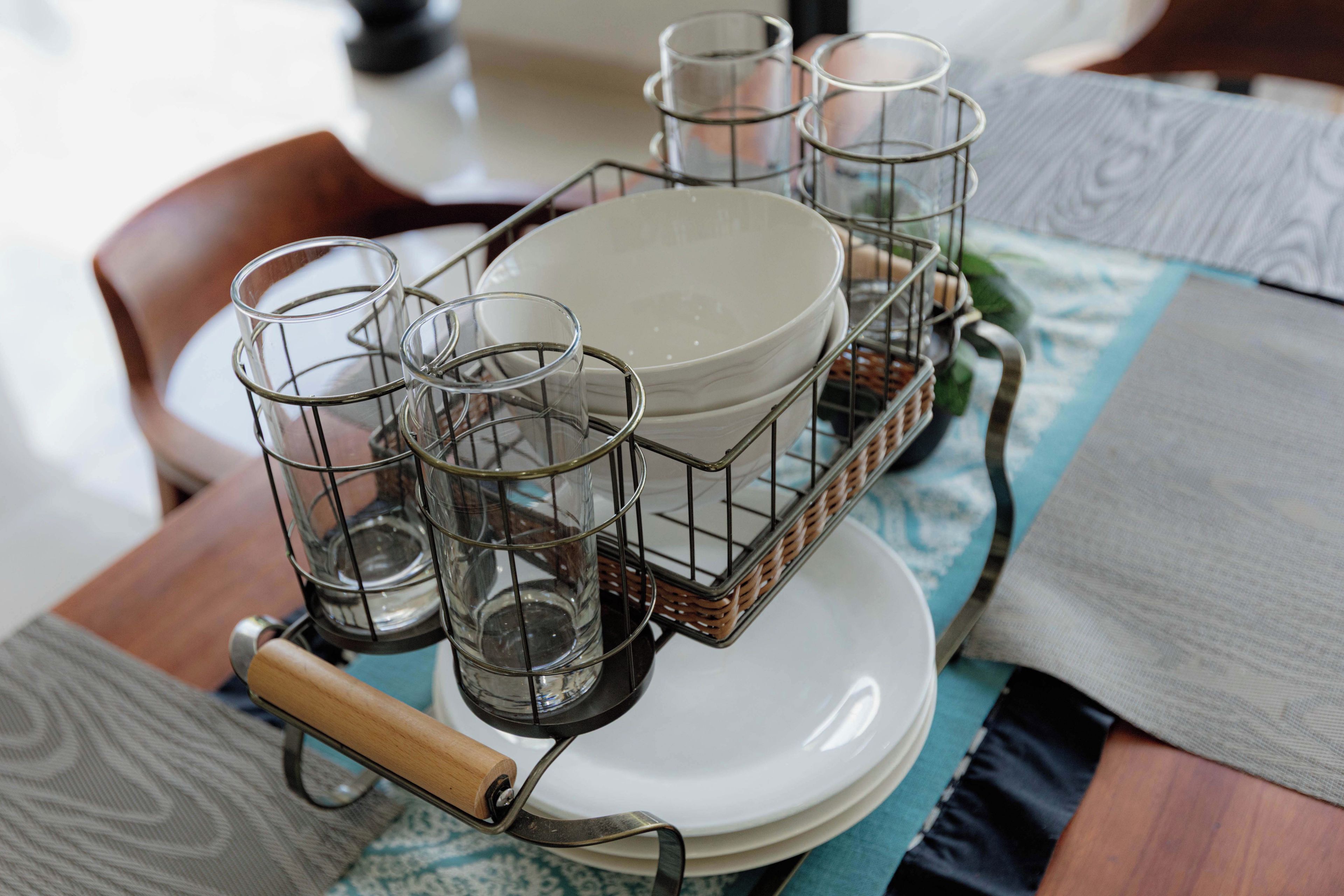 Un tavolo da pranzo con un porta bicchieri metallico che contiene diversi bicchieri trasparenti e un piatto bianco.