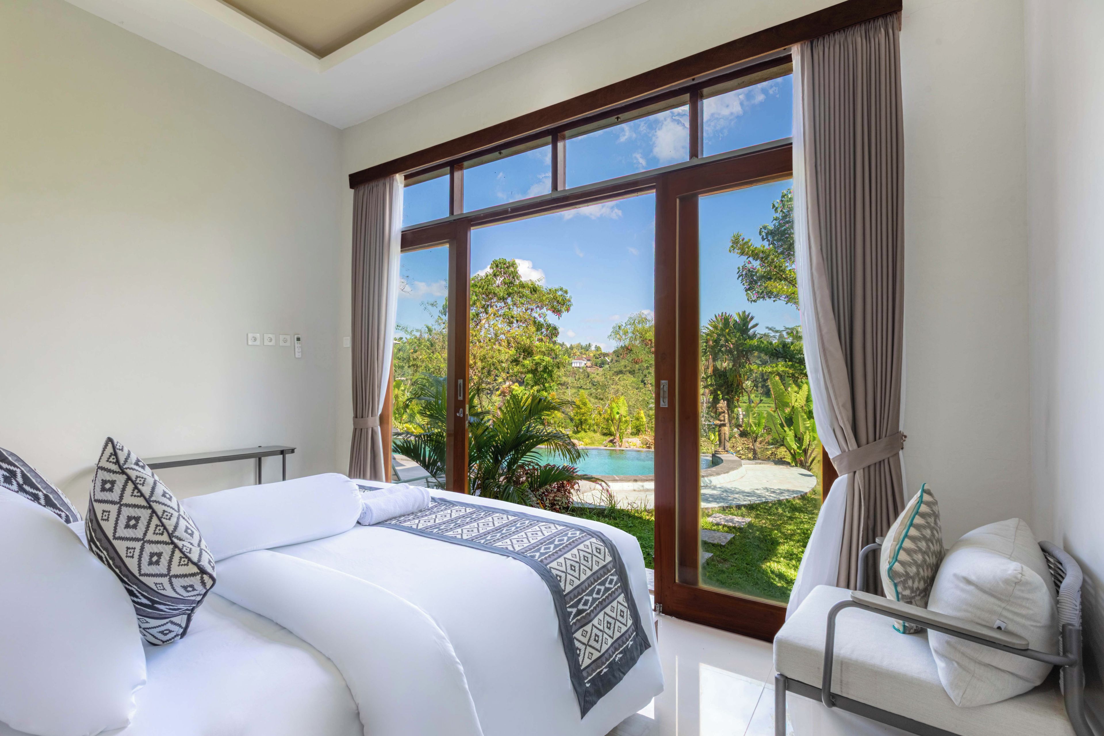 Ein Hotelzimmer mit einem Bett, einem Sessel und Blick auf einen Pool und Grünflächen.