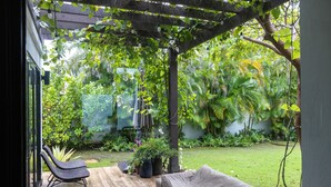 Un patio techado con cubierta de madera, un espacio de estar al aire libre cubierto y abundante vegetación al fondo.