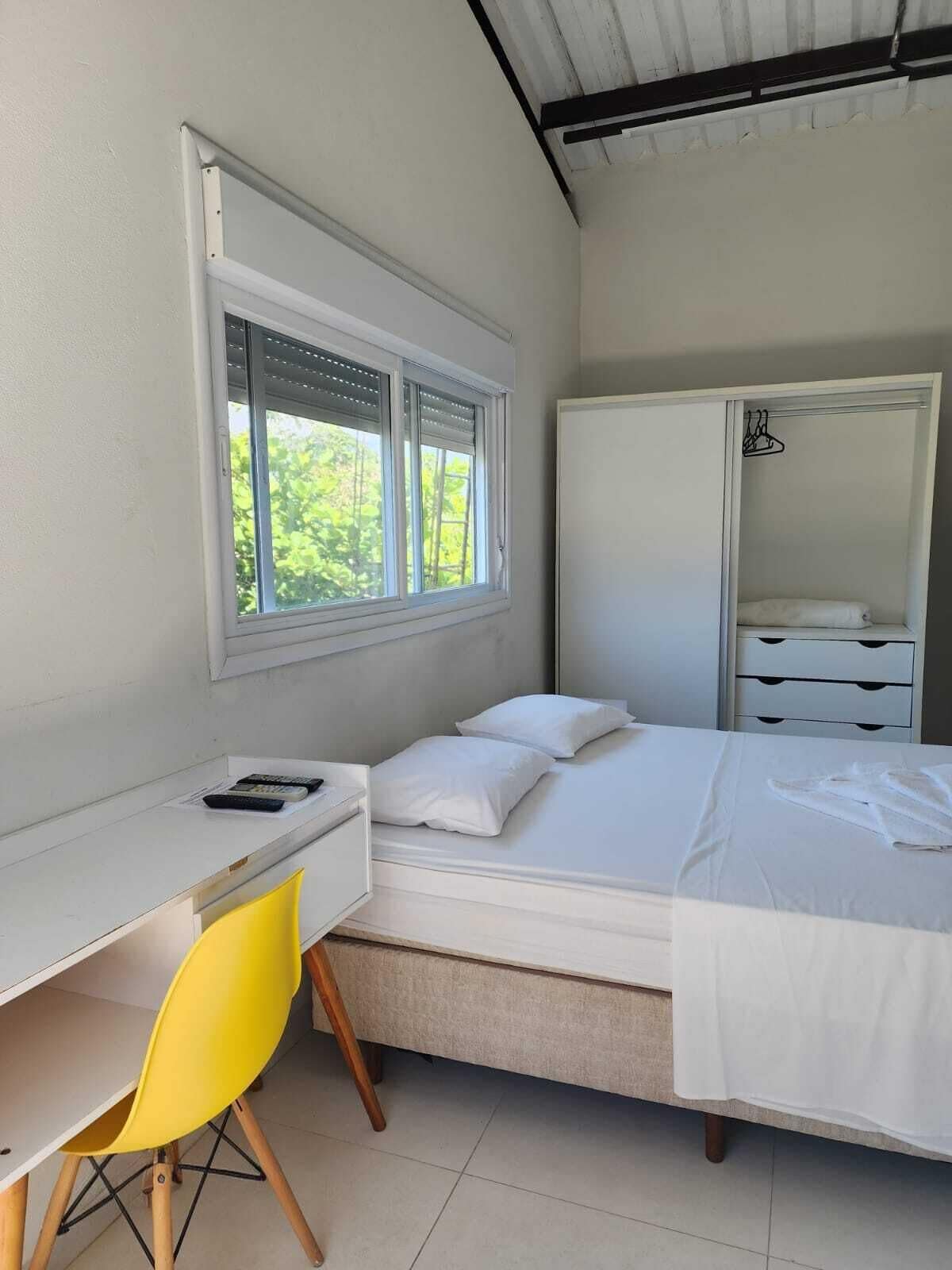 Un dormitorio con cama, escritorio, silla, armario y ventana con persianas.