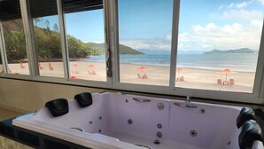 Ein Badezimmer mit einer großen Badewanne, einem Fenster mit Blick auf einen Strand und gefliesten Wänden.