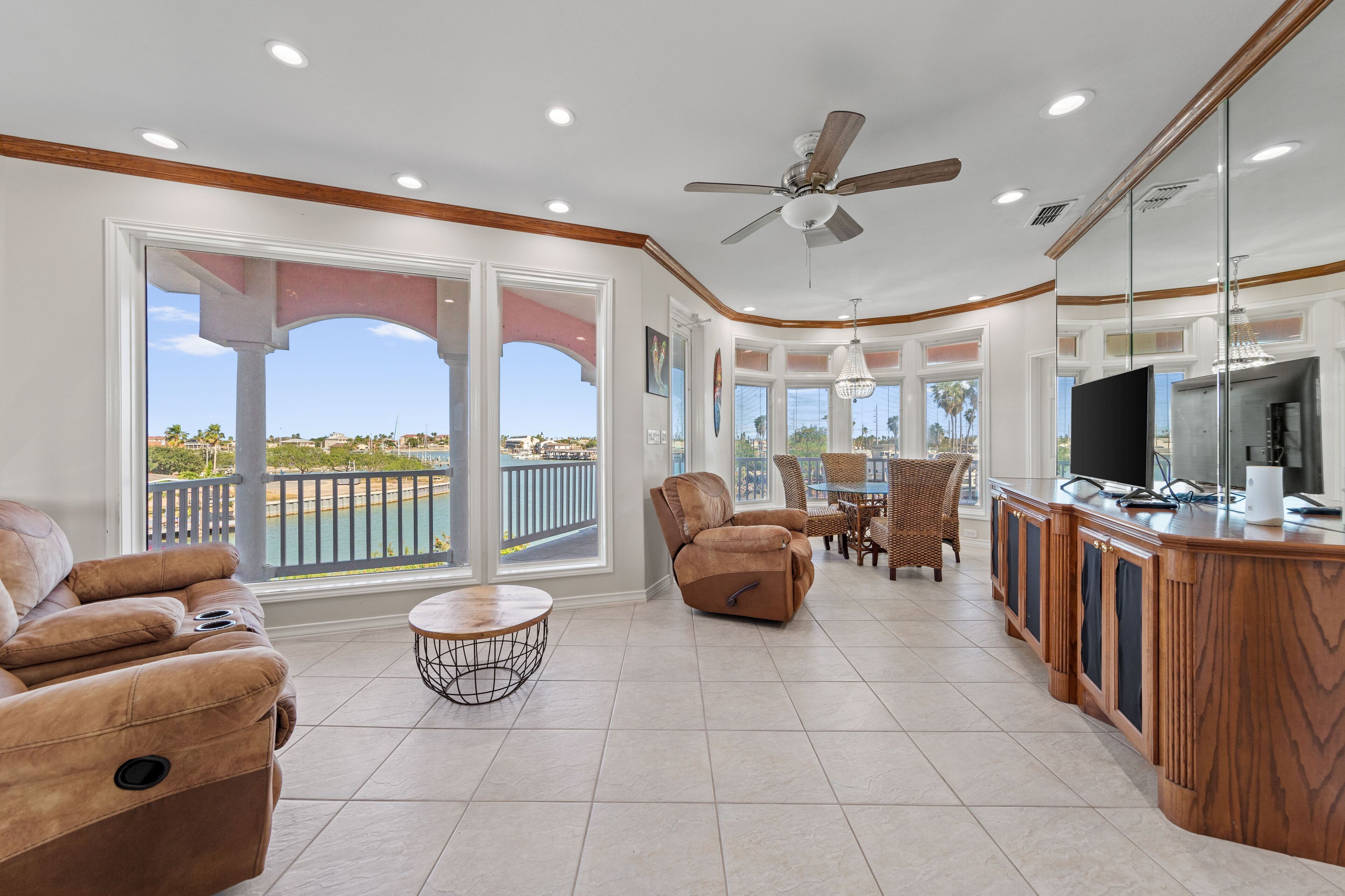 A spacious living area with a balcony, a ceiling fan, and a kitchen area with a bar.