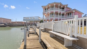 A wooden pier leading to a pink and white building with balconies, a white fence, and a clear sky. - Pelican Point Bay on the Water, Boat Slips, View! (Port Isabel)
