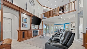 A spacious living room with a large flat-screen TV, leather recliners, a wooden entertainment center, and a staircase leading to an upper level. - Pelican Point Bay on the Water, Boat Slips, View! (Port Isabel)