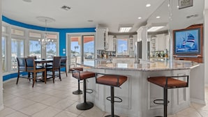 A modern kitchen with a central island, bar stools, and a dining area with chairs. - Pelican Point Bay on the Water, Boat Slips, View! (Port Isabel)