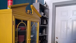 Um armário amarelo com portas de vidro, um extintor por cima e um tapete listrado no chão.