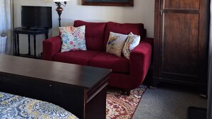 Um quarto com sofá vermelho, televisão sobre um suporte, pintura de baleias, armário de madeira e tapete estampado.