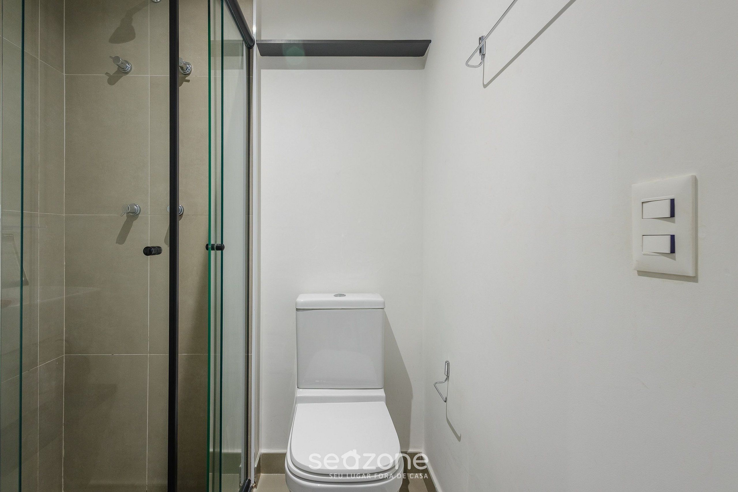 Un bagno con cabina doccia in vetro, un water bianco e un interruttore luce a parete.