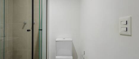 A bathroom with a glass shower enclosure, a white toilet, and a wall-mounted light switch.