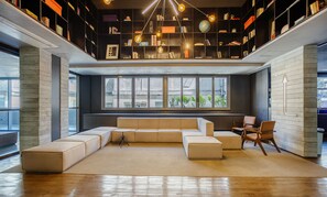 A modern living room with a sectional sofa, a coffee table, and a bookshelf filled with books and decorative items. - Your Complete Stay in a Building With a Pool Just Steps From the Subway - FRE (São Paulo)