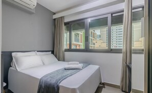 A hotel room with a bed, a window with curtains, and a view of buildings outside. - Your Complete Stay in a Building With a Pool Just Steps From the Subway - FRE (São Paulo)