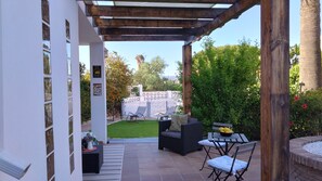 An outdoor patio area with a pergola, seating, and a view of a garden and pool.
