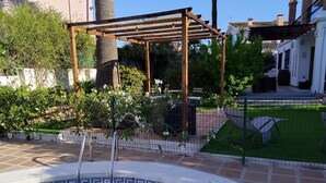 Ein Schwimmbecken mit einer Holzpergola, umgeben von einem Zaun und Grünpflanzen.