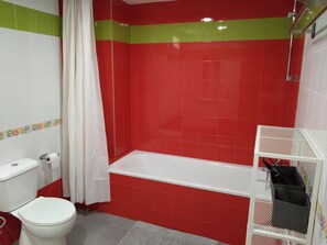 A bathroom with red and white tiles, a white bathtub, a toilet, and a shower area.