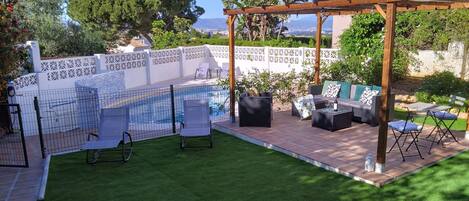 Un patio trasero con piscina, mobiliario exterior y una pérgola.