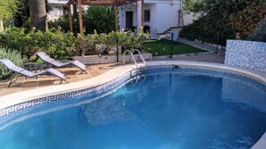 A swimming pool with a tiled edge, lounge chairs, and a pergola structure.