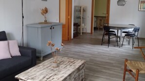 Ein Wohnzimmer mit einem dunklen Sofa, einem rustikalen Couchtisch und einem blauen Schrank. Im Hintergrund befindet sich ein Essbereich mit Tisch und Stühlen.
