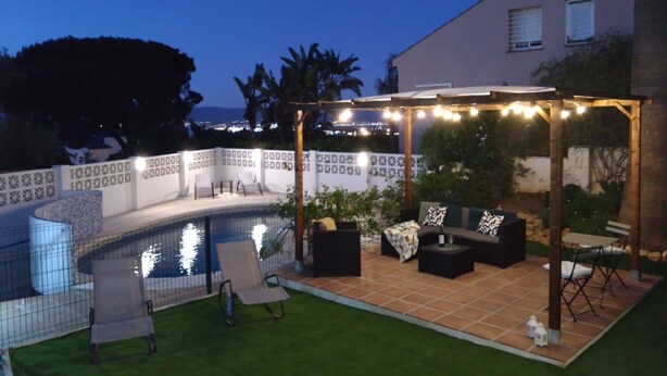 Ein Garten mit Swimmingpool, Sitzgelegenheiten im Freien und einer Pergola mit Lichterkette.