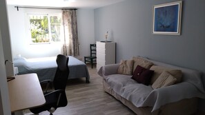 A bedroom with a bed, a desk, a chair, a dresser, a couch, and a painting on the wall.