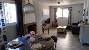 Ein Essbereich mit Tisch für vier Personen, einem Kamin und einem Wohnzimmer mit Sofa und Fernseher.
