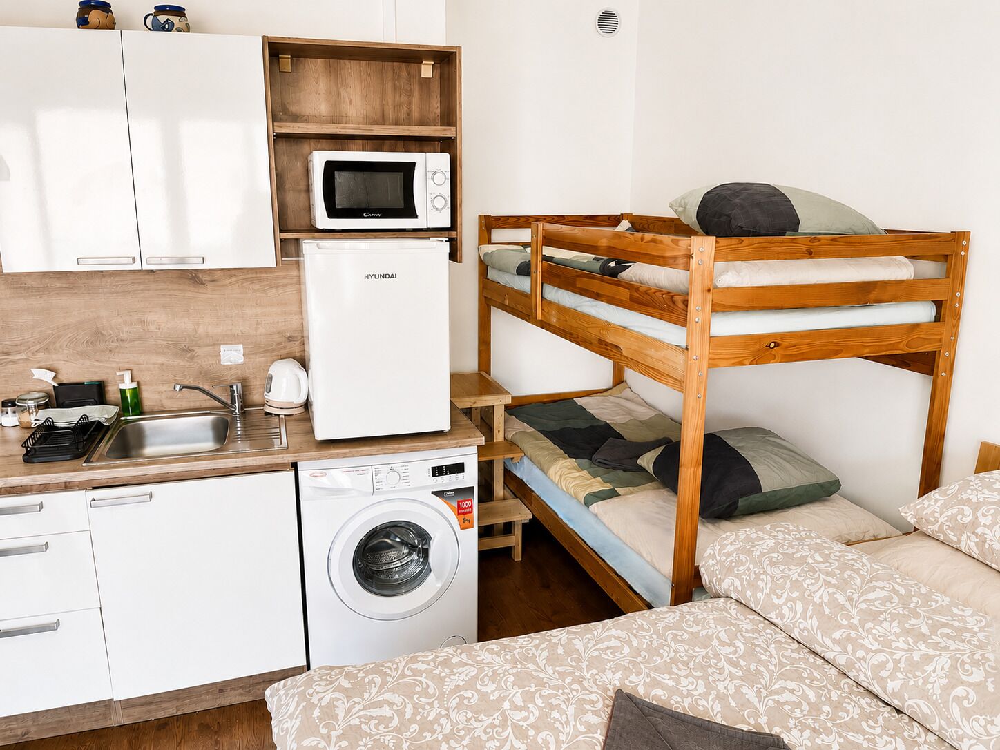 A compact kitchenette with a microwave, refrigerator, sink, and washing machine.