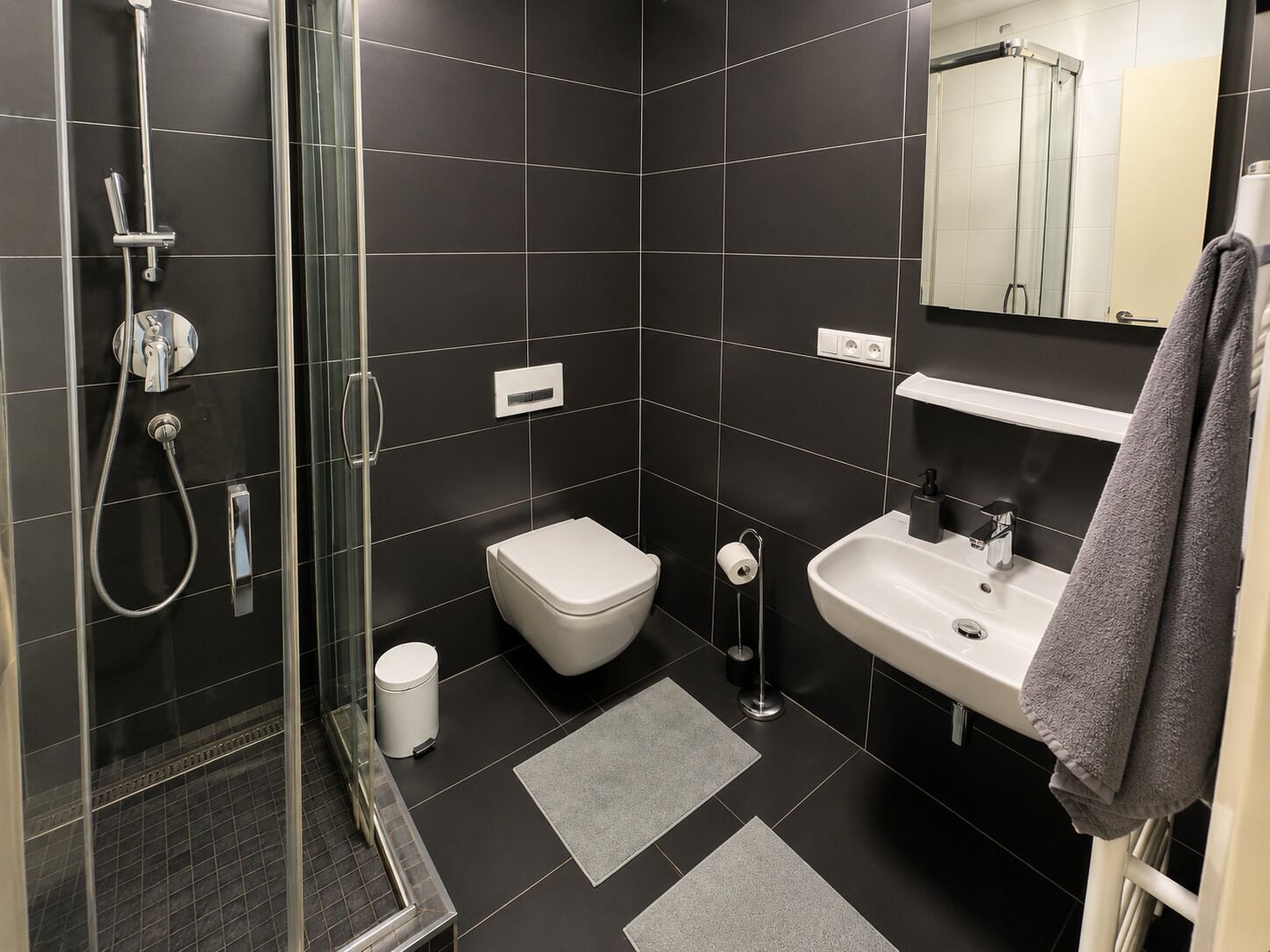 A modern bathroom with a glass-enclosed shower, a white toilet, a sink, and a towel rack.
