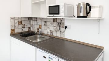 Een koelkast, een magnetron, een kookplaat, kookgerei, borden en bestek