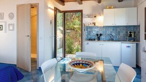 A modern kitchen with white cabinets, a blue tiled backsplash, and a glass dining table.