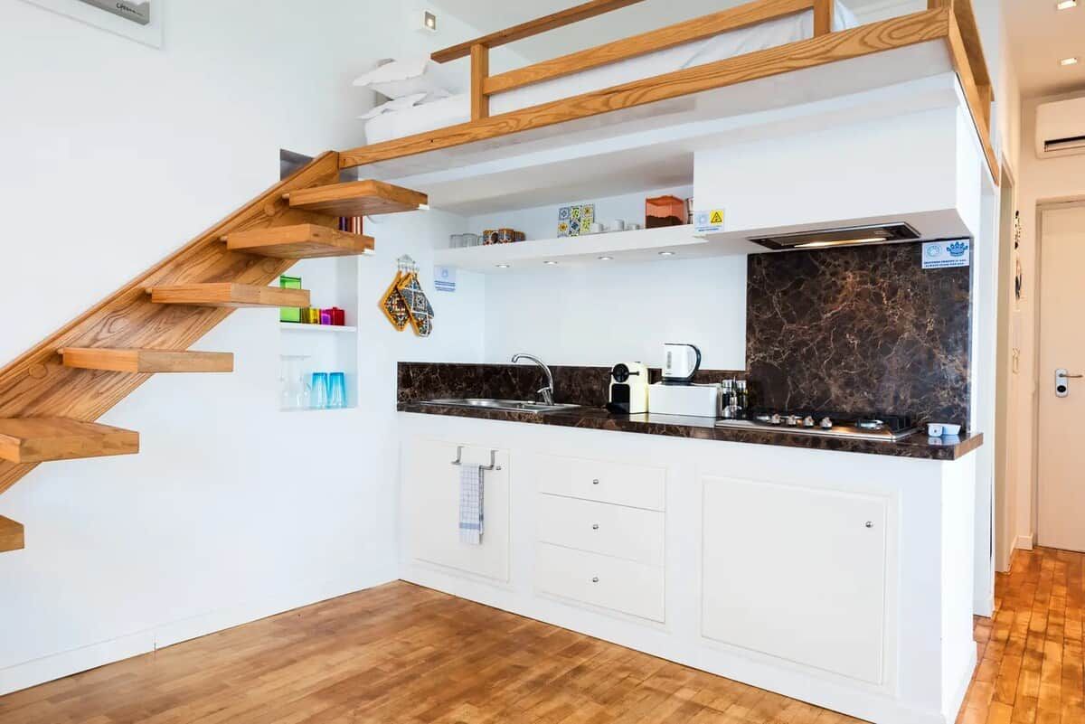 Une cuisine avec un escalier en bois, des armoires blanches et un plan de travail en marbre.