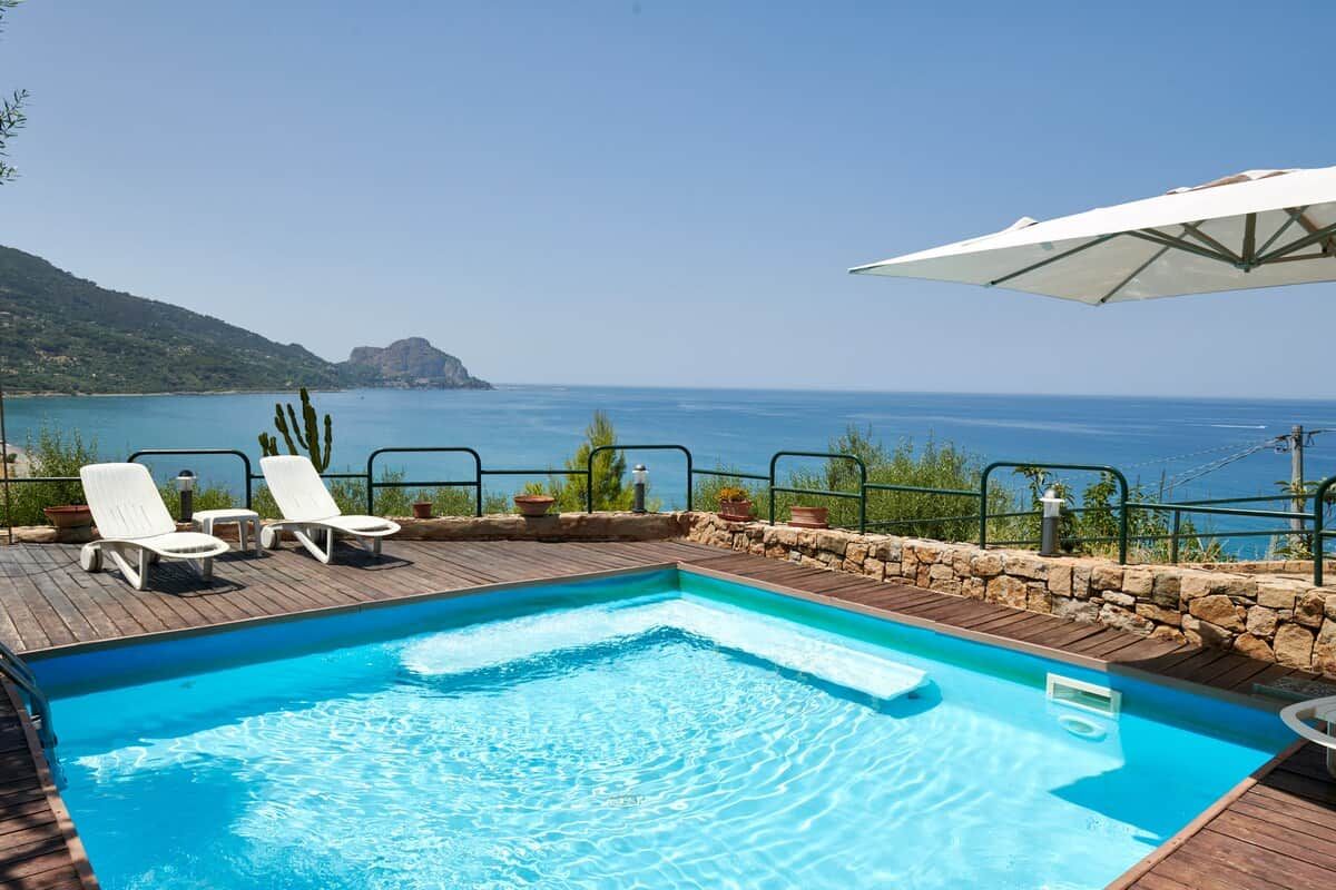 A swimming pool with lounge chairs and an umbrella, overlooking a body of water.