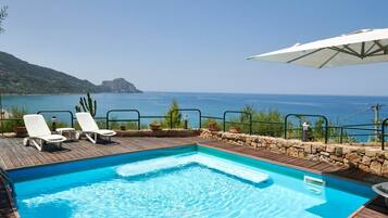 A swimming pool with lounge chairs and an umbrella, overlooking a body of water.
