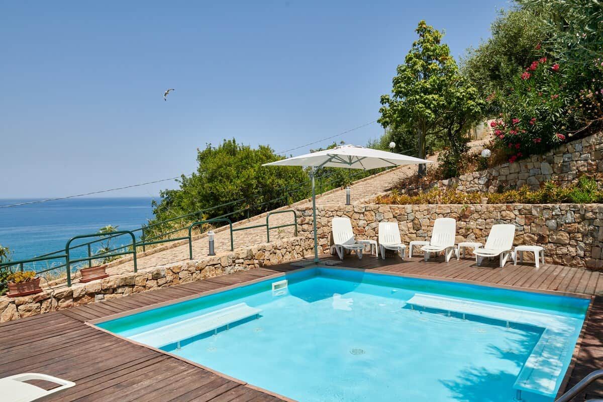 A swimming pool with lounge chairs and a stone wall, overlooking a body of water.