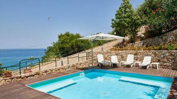 A swimming pool with lounge chairs and a stone wall, overlooking a body of water.